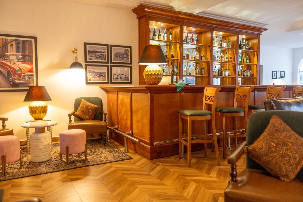 The back bar of the 1950s Bar: a timber counter and stools, lit bottle shelves, table lamps and framed archive prints.