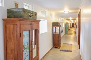 A guest corridor with framed pictures, a timber cabinet and a chequerboard floor.