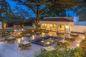 Outdoor tables lit by candles on the courtyard terrace at blue hour, arcades glowing behind.