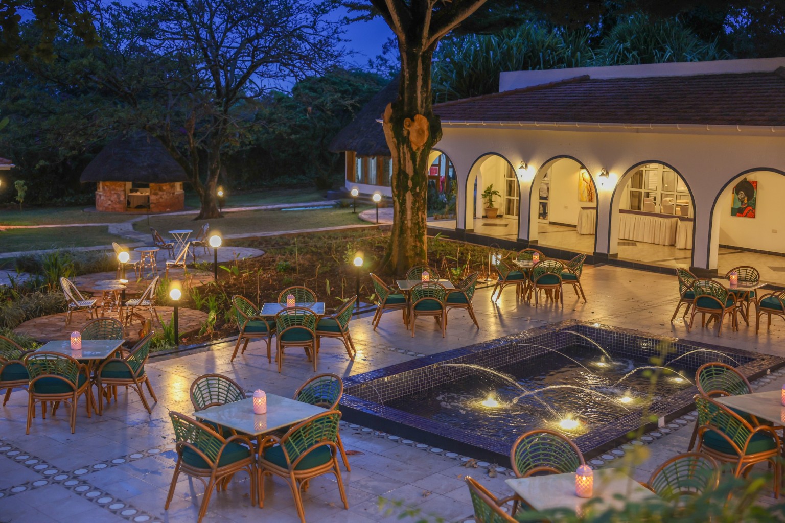 Cane chairs and tables set out across the paved courtyard terrace in the evening.