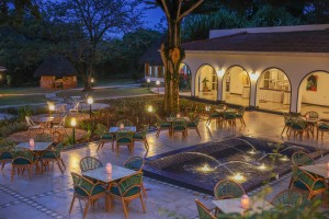 Cane chairs and tables set out across the paved courtyard terrace in the evening.