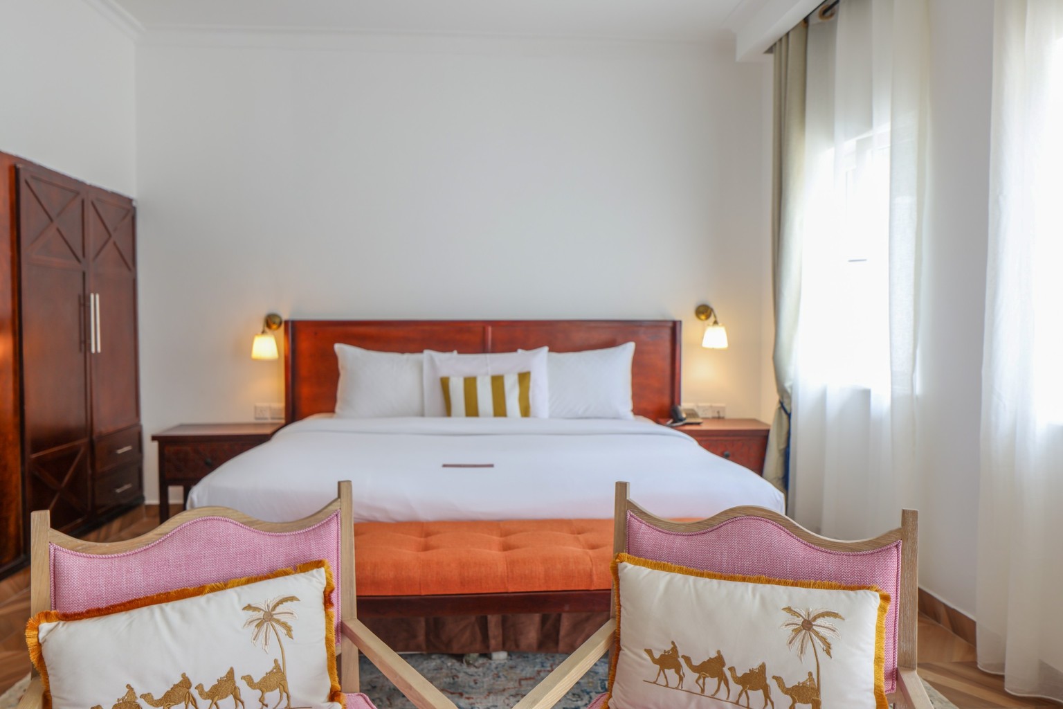 A king bed with white linen, upholstered bench and fitted timber wardrobe.