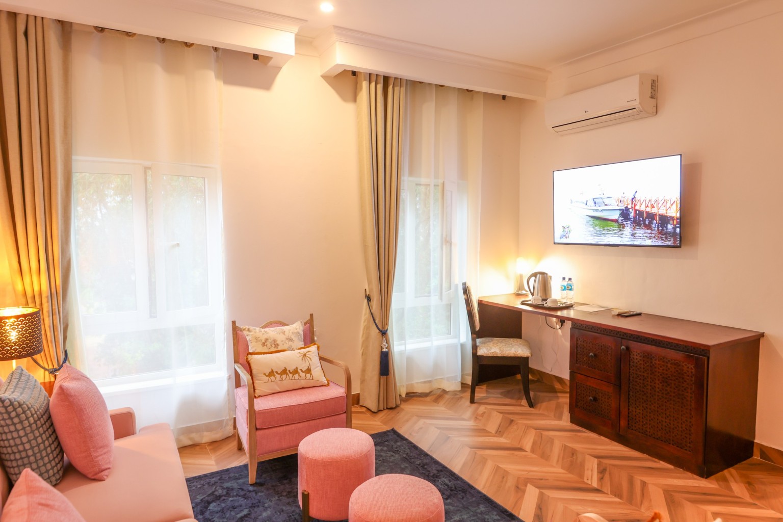 Deluxe Room seating area with armchair, desk and television, curtains open to daylight.