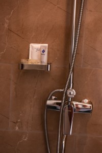 A shower with handset and toiletries in a marble-tiled bathroom.