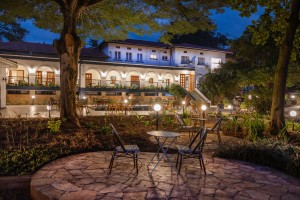 Cafe tables set on a paved circle in the lawned courtyard, the arcaded wings of the hotel behind.