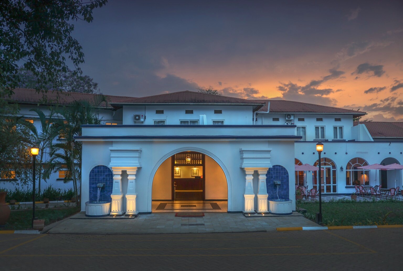 The hotel’s white 1950s facade at dusk, its central arch lit gold beneath a violet sky.