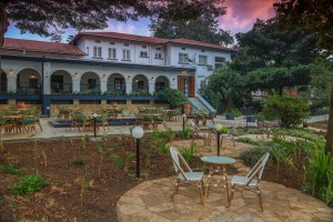 A pair of chairs and a small table on a paved garden circle, the hotel lit behind at dusk.