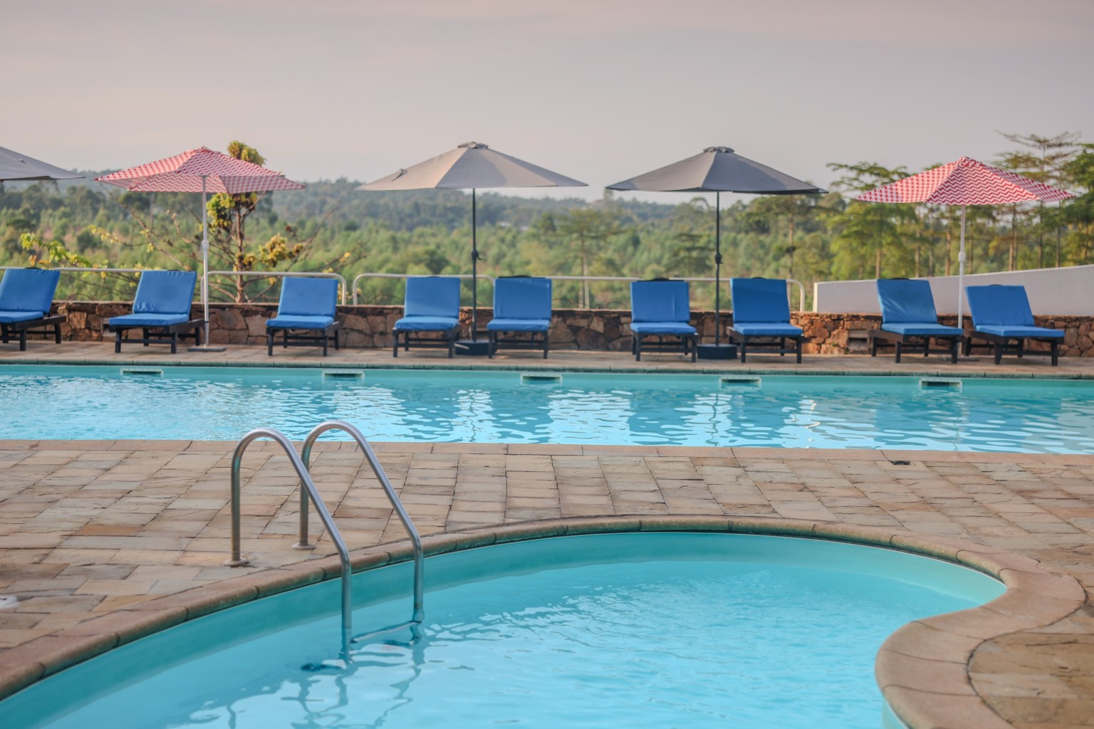 The pool and its paved terrace with parasols, hills in the distance.