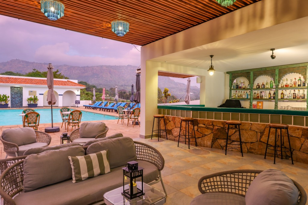 The open-sided Roots Bar under a slatted timber ceiling, its stone counter and cane seating looking out to the pool and the hills.