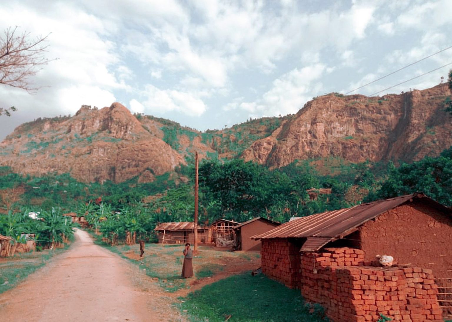 A dirt road through a village below the rocky cliffs that rise behind Mbale.
