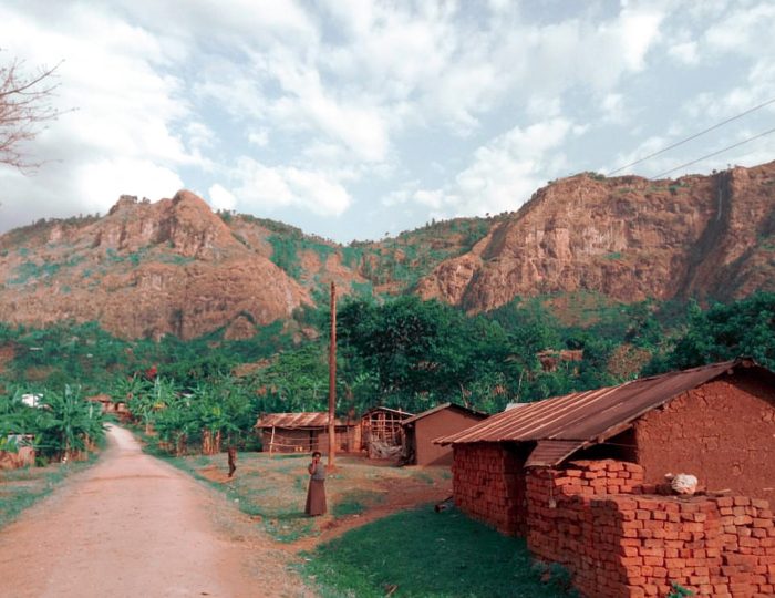 A dirt road through a village below the rocky cliffs that rise behind Mbale.