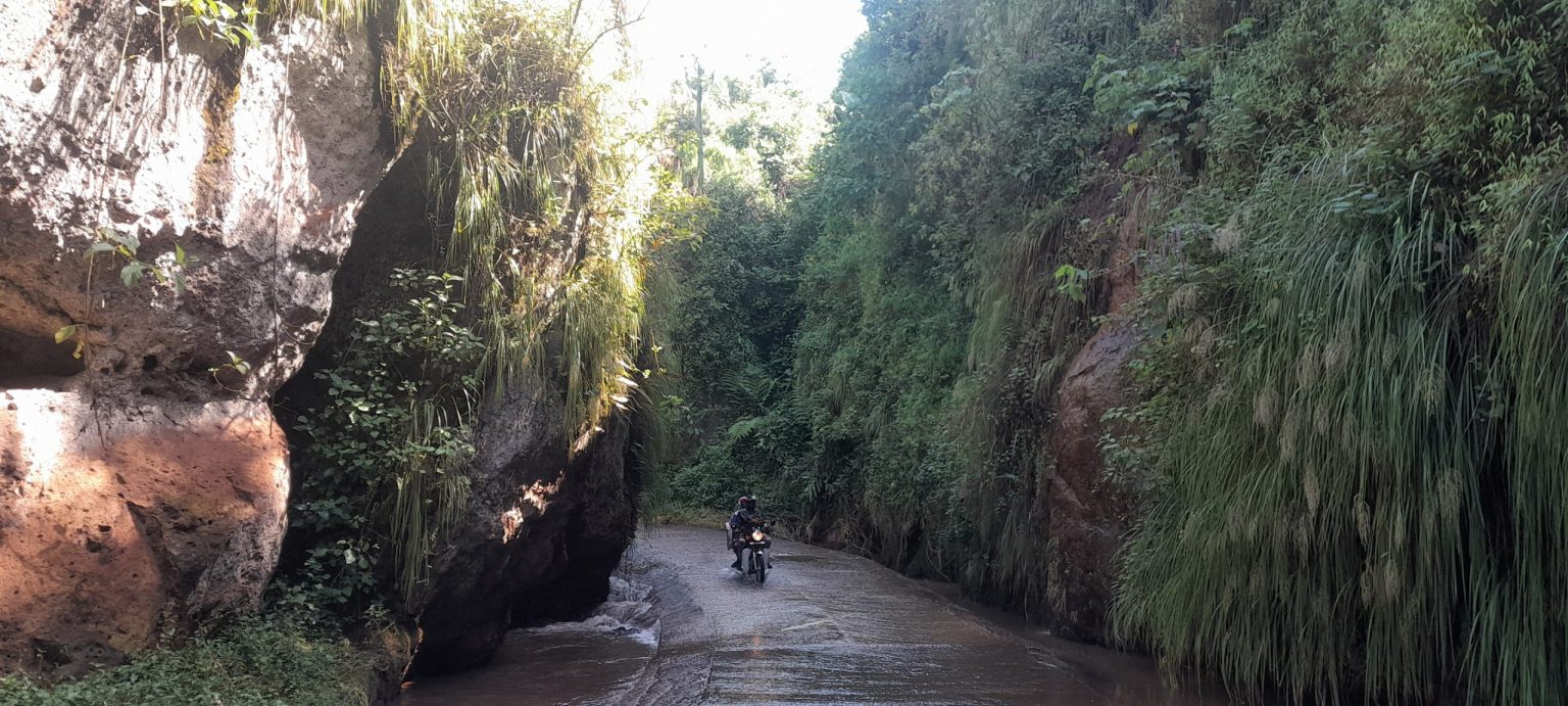 A motorcycle on a wet track running through a narrow rock gorge in eastern Uganda.