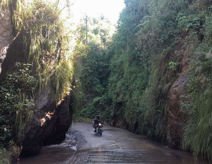 A motorcycle on a wet track running through a narrow rock gorge in eastern Uganda.