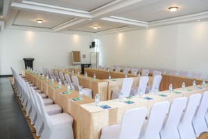 The conference hall dressed for a session, with covered chairs, notepads and water set out.