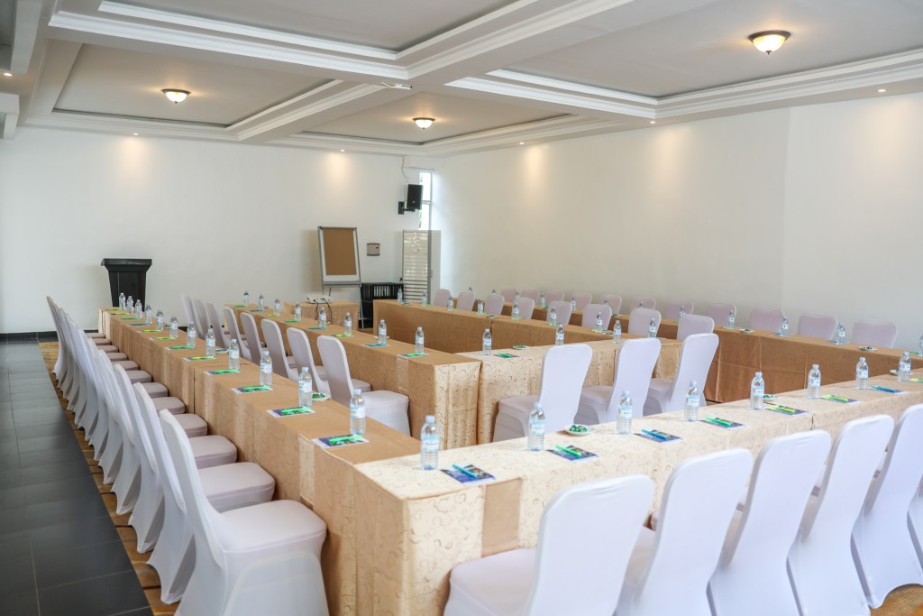 A conference hall set classroom style, rows of skirted tables and white covered chairs facing the front of the room.