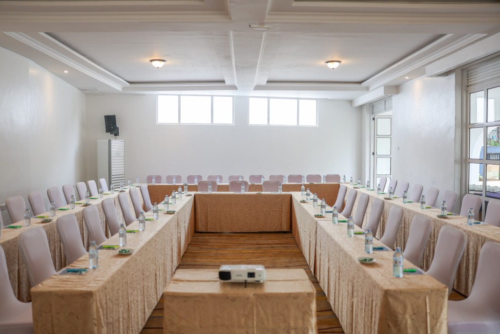 The conference hall dressed in a hollow rectangle, skirted tables and covered chairs with notepads, water and a projector set out.