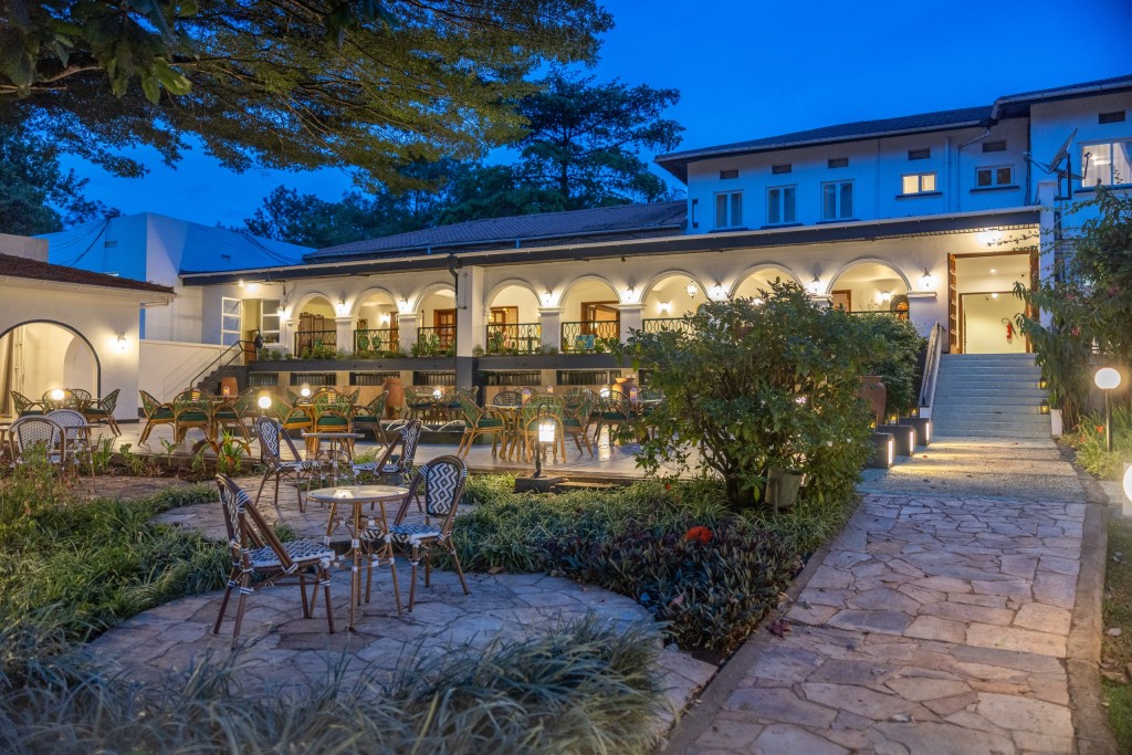 The courtyard at blue hour, garden beds and seating in the foreground and the lit arcades running round three sides.
