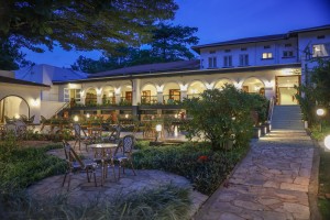 Candlelit tables and a lit water feature on the courtyard terrace at blue hour, the arcades glowing behind.