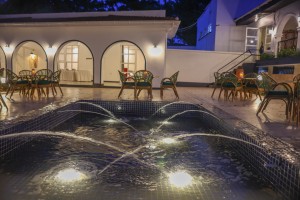 Candlelit tables and a lit water feature on the courtyard terrace at blue hour, the arcades glowing behind.