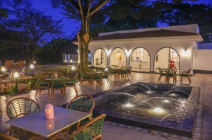 Candlelit tables and a lit water feature on the courtyard terrace at blue hour, the arcades glowing behind.