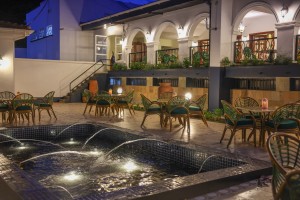 Candlelit tables and a lit water feature on the courtyard terrace at blue hour, the arcades glowing behind.