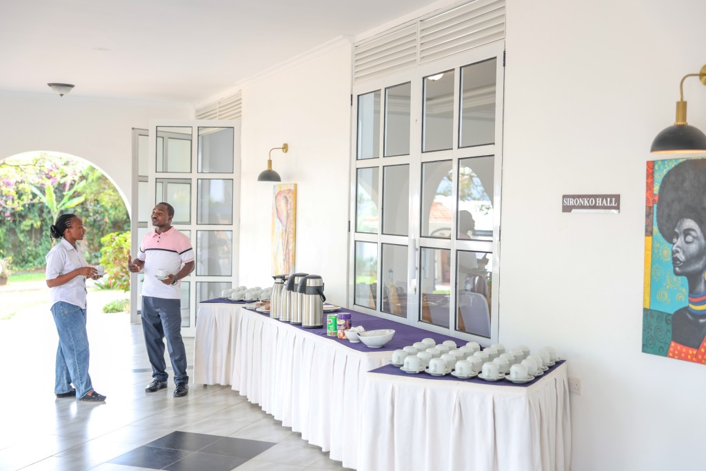 A wide view of the break room, two delegates talking near a long refreshment table set with cups.
