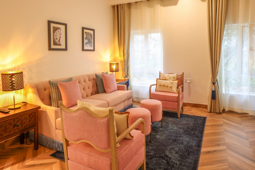 A suite sitting room with a pink sofa, armchairs and a writing desk under framed prints.