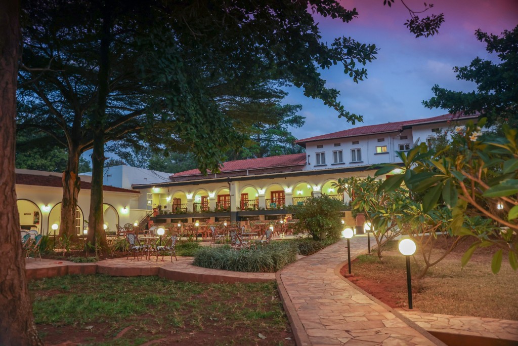 A stone path curving through the hotel gardens between mature trees, lamps lit along it at dusk.