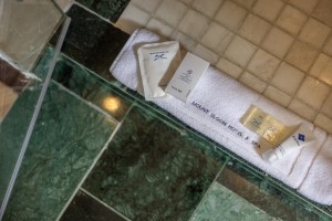 An en-suite bathroom with basin, mirror and a glazed shower, tiled in green marble.