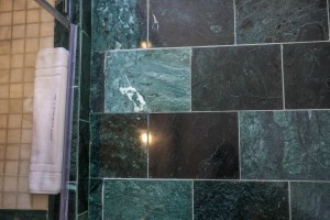 An en-suite bathroom with basin, mirror and a glazed shower, tiled in green marble.