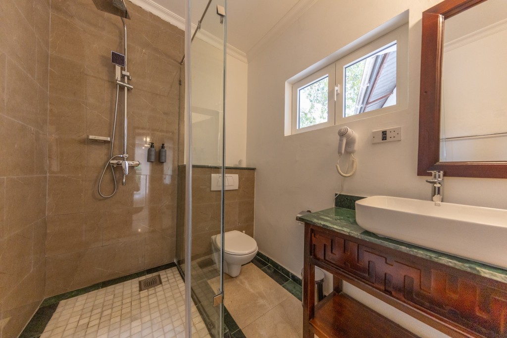 An en-suite bathroom with a glazed walk-in shower, a basin set into a dark timber washstand and a green marble surround.