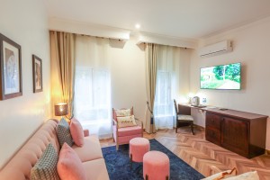 A guest room with sofa seating, writing desk, television and a window onto the garden.