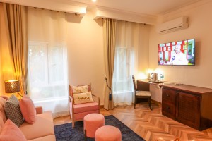 A guest room with sofa seating, writing desk, television and a window onto the garden.