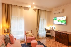A guest room with sofa seating, writing desk, television and a window onto the garden.
