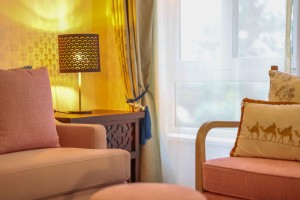 A guest room with sofa seating, writing desk, television and a window onto the garden.