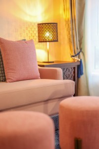 A guest room with sofa seating, writing desk, television and a window onto the garden.