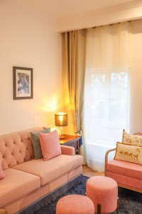 A guest room with sofa seating, writing desk, television and a window onto the garden.