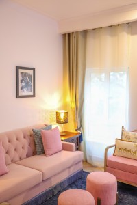 A guest room with sofa seating, writing desk, television and a window onto the garden.