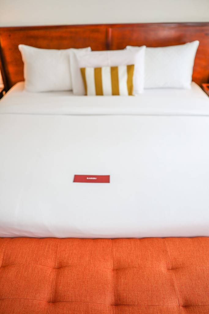 A close view of a made bed, white linen turned down over a deep orange base.