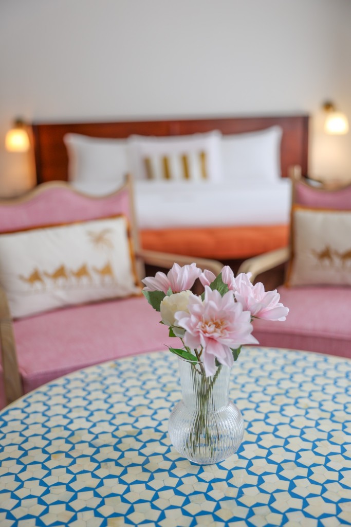 Twin beds made up side by side with a vase of flowers on the round table in front of them.