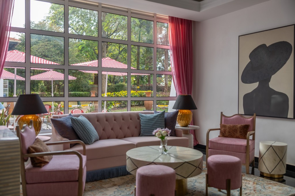 A long buttoned sofa and armchairs in the lobby lounge, set beneath a wall of tall windows looking out to the garden.