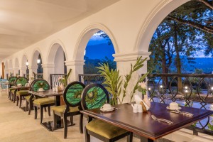 Masaaba Restaurant: tables and cane chairs along the arched veranda, hills and greenery through the openings.