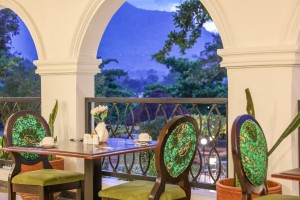 Masaaba Restaurant: tables and cane chairs along the arched veranda, hills and greenery through the openings.