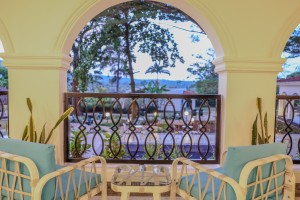 Masaaba Restaurant: tables and cane chairs along the arched veranda, hills and greenery through the openings.