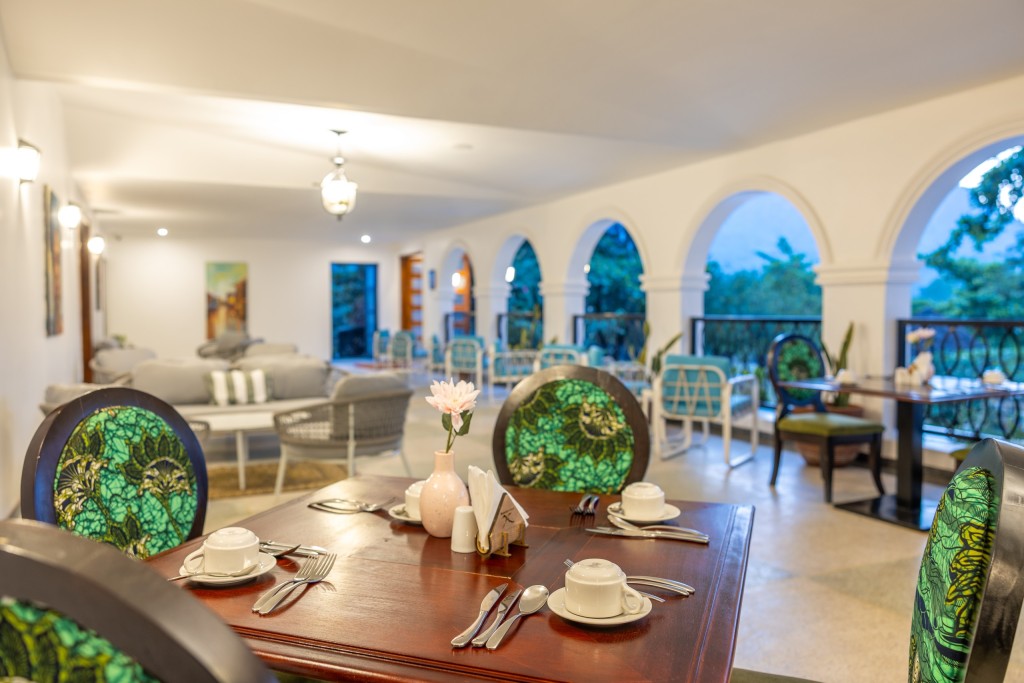 A laid table in the long arcaded dining room, arches open to the garden and further tables receding beyond it.