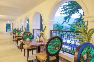 Masaaba Restaurant: tables and cane chairs along the arched veranda, hills and greenery through the openings.