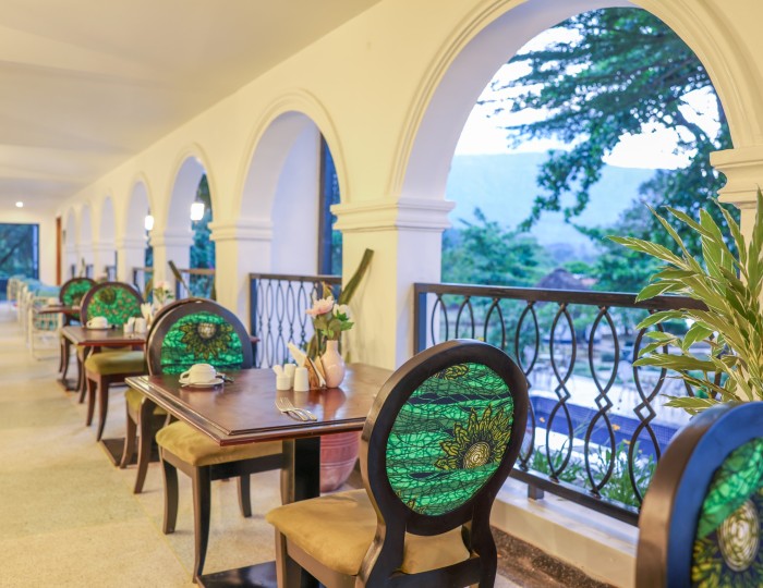 A laid table beside the tall arches of Masaaba Restaurant, looking out over the trees to the hills.
