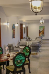 Masaaba Restaurant: tables and cane chairs along the arched veranda, hills and greenery through the openings.