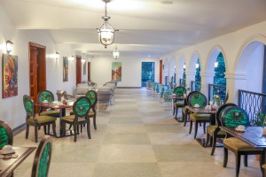 Masaaba Restaurant: tables and cane chairs along the arched veranda, hills and greenery through the openings.