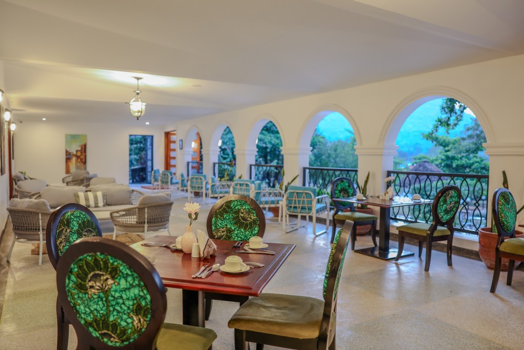 Tables laid along the arcaded dining room, arches open to the trees and lounge seating beyond.